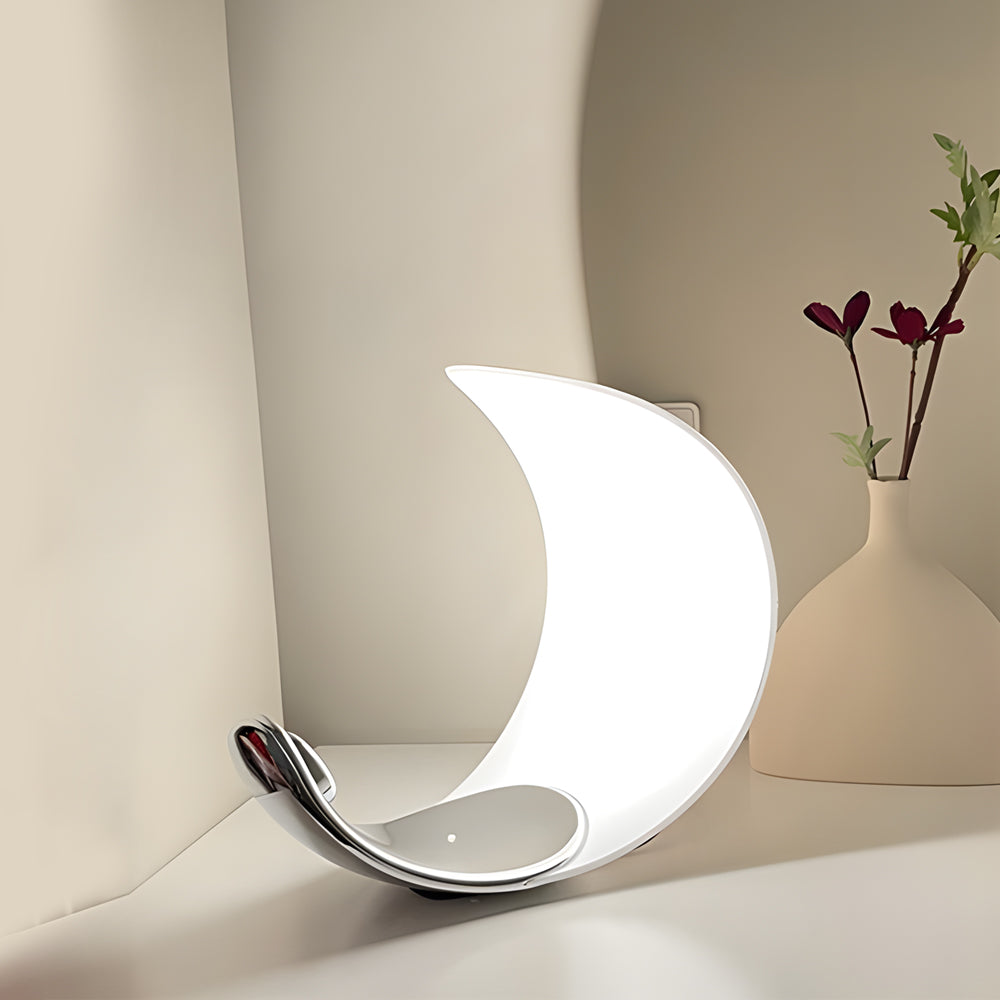 Curved silver end table lamp with a contemporary design, placed beside a white wall.