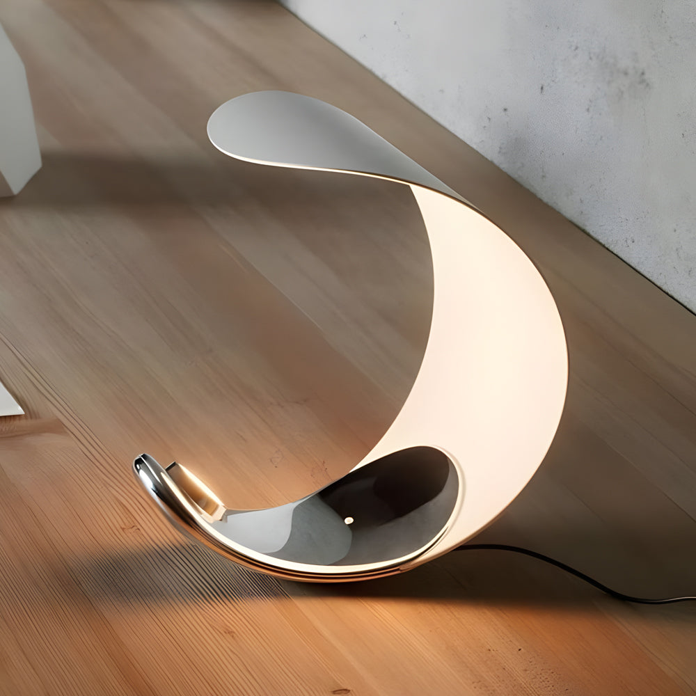 Curved silver end table lamp with a minimalist design, placed on a wooden floor.