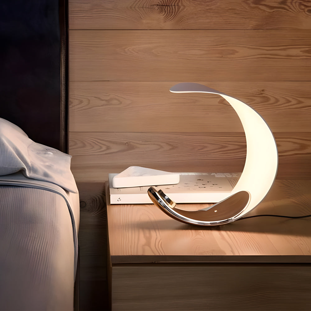 Curved silver end table lamp with a modern design, placed on a bedside table.