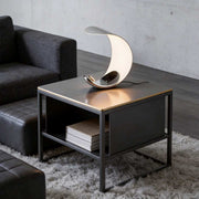 Curved silver end table lamp with a modern design, placed on a black side table.