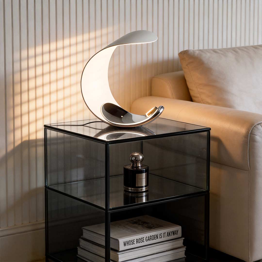Curved silver end table lamp with a sleek design, illuminating a glass side table.