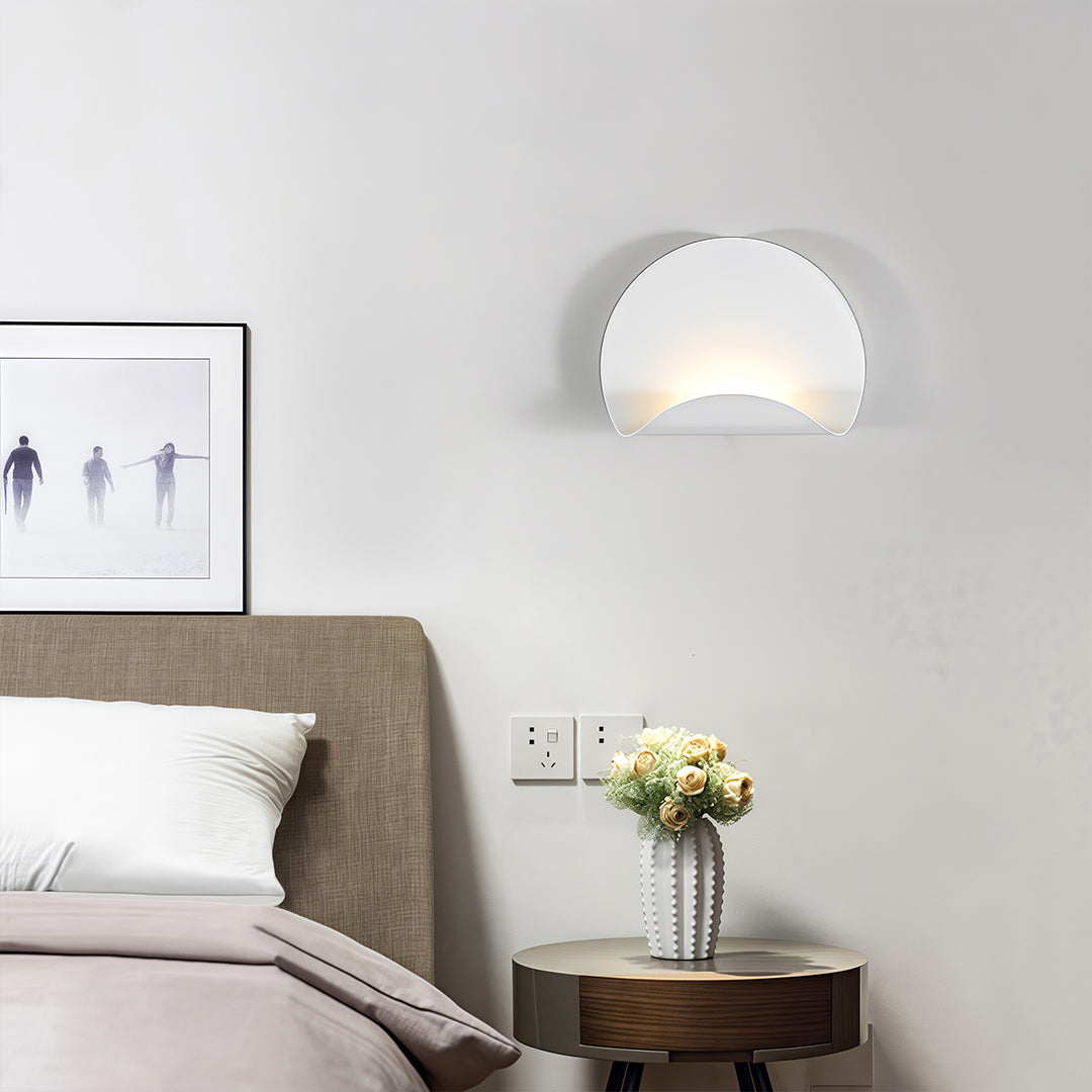 Curved white wall lights providing soft, indirect up-and-down lighting beside a bed in a hotel-style room.
