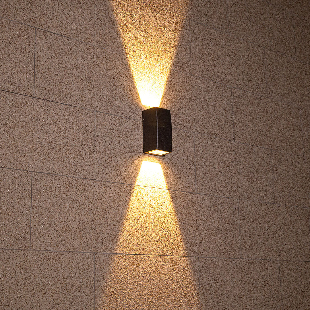Modern black outdoor light producing brilliant warm illumination against rich textured wall