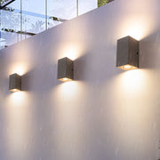 Multiple concrete wall lights installed on modern building facade creating dramatic up-down lighting