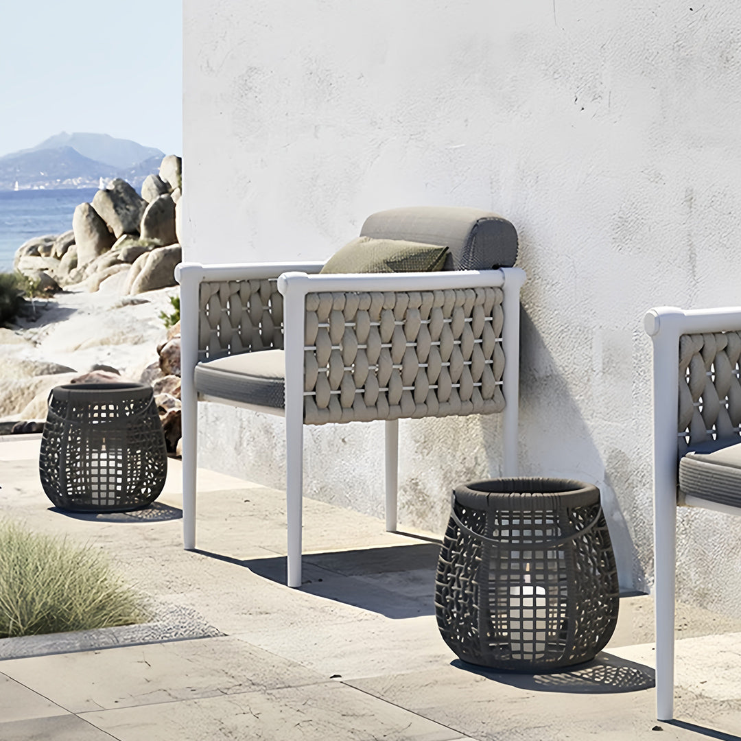 Dark gray woven outdoor lanterns on a seaside patio with contemporary furniture, showcasing the weatherproof material and clean design.