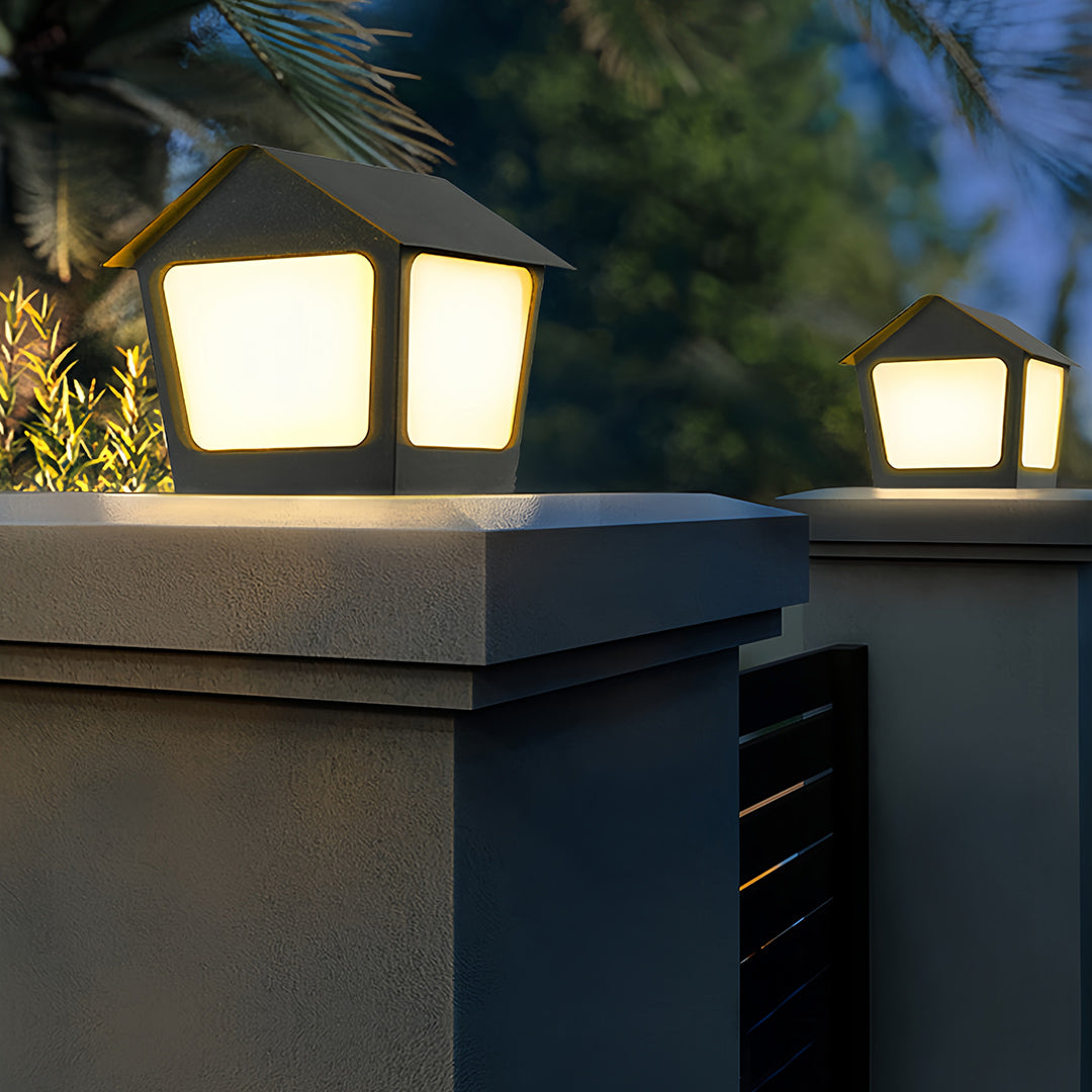 Two dark metal deck post cap lights mounted on a thick concrete wall, creating clear boundary lighting near a modern house.