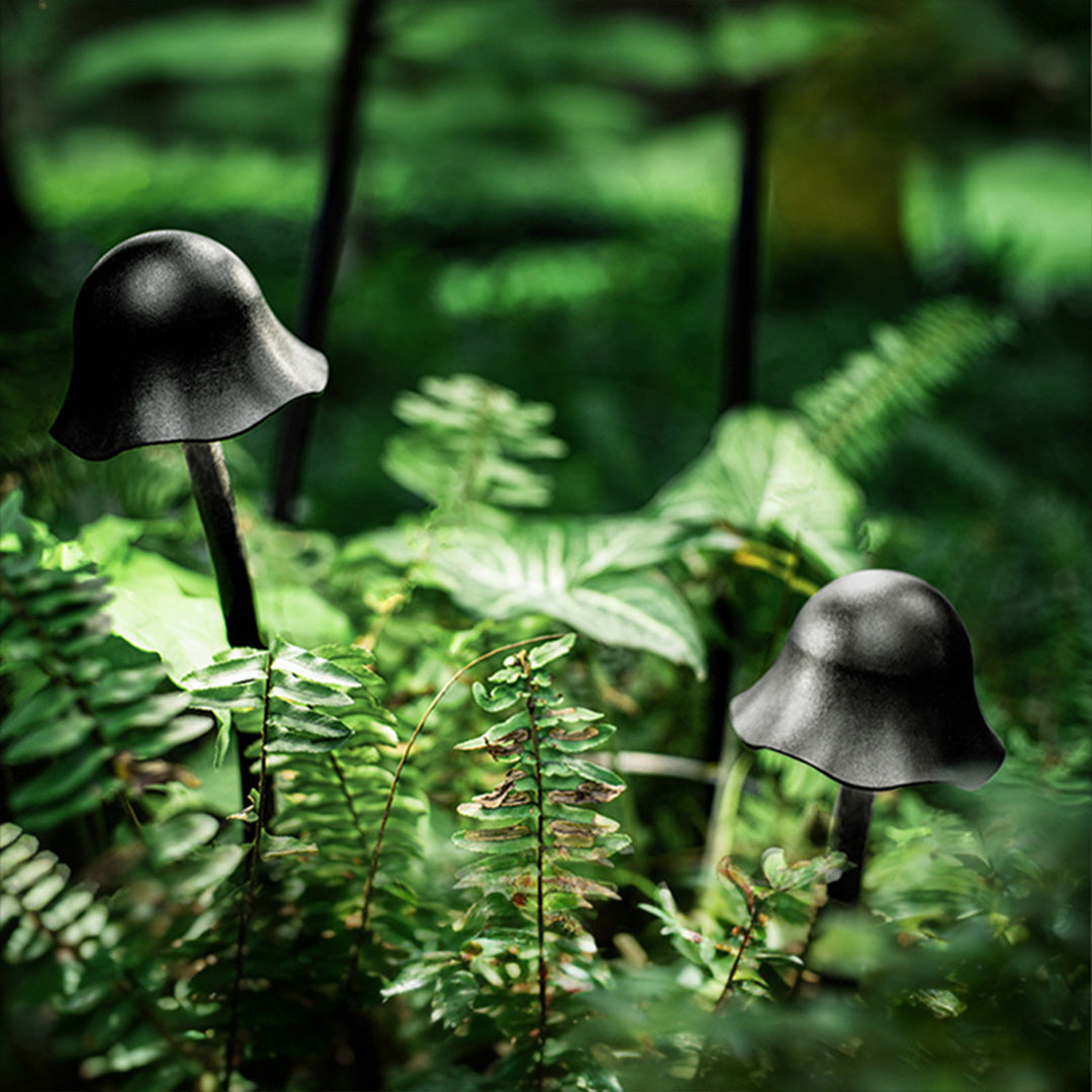 Dark outdoor landscape light fixtures arranged among ferns and moss creating atmospheric forest lighting