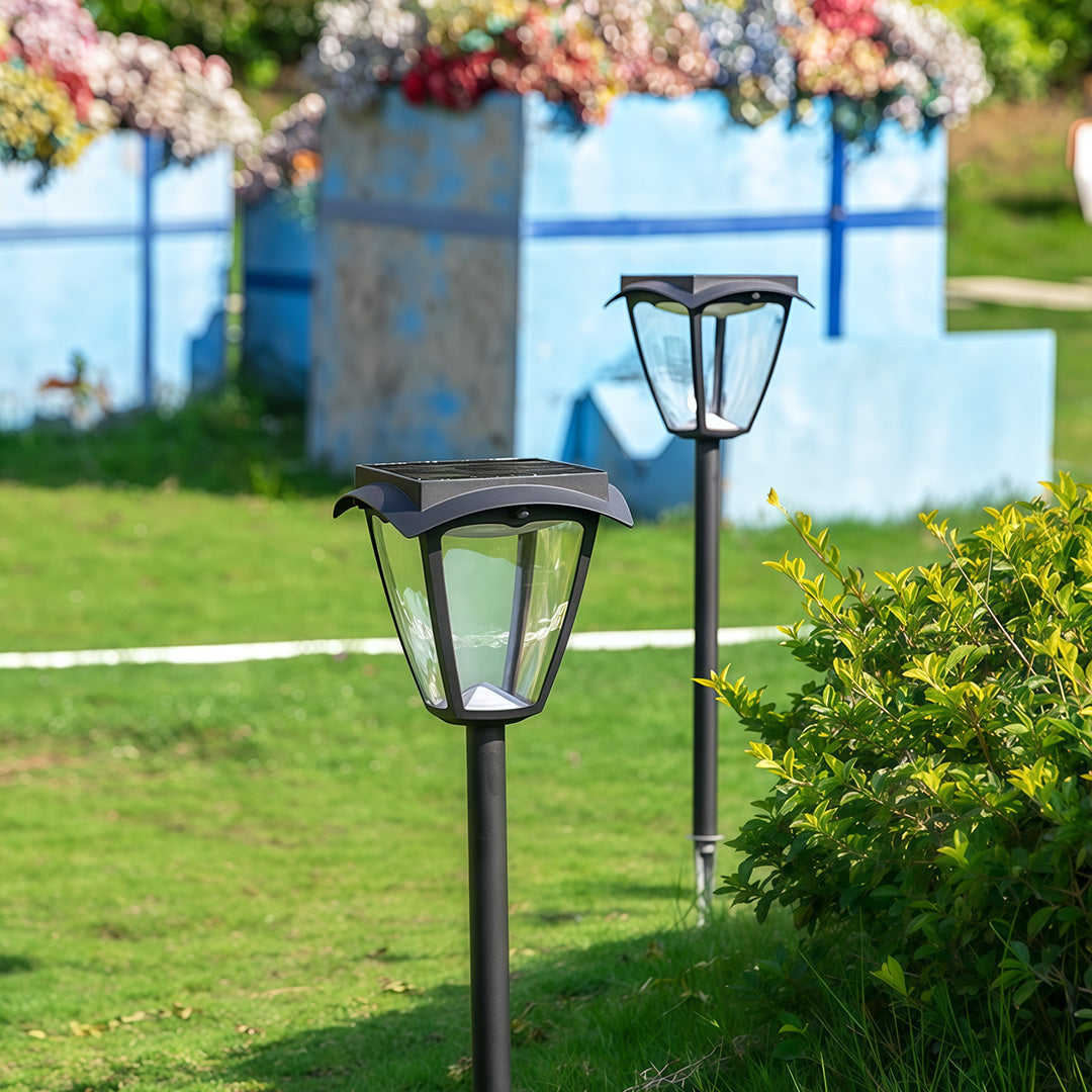 Daytime view of classic lantern-style solar powered path lighting stakes installed in a green garden lawn.
