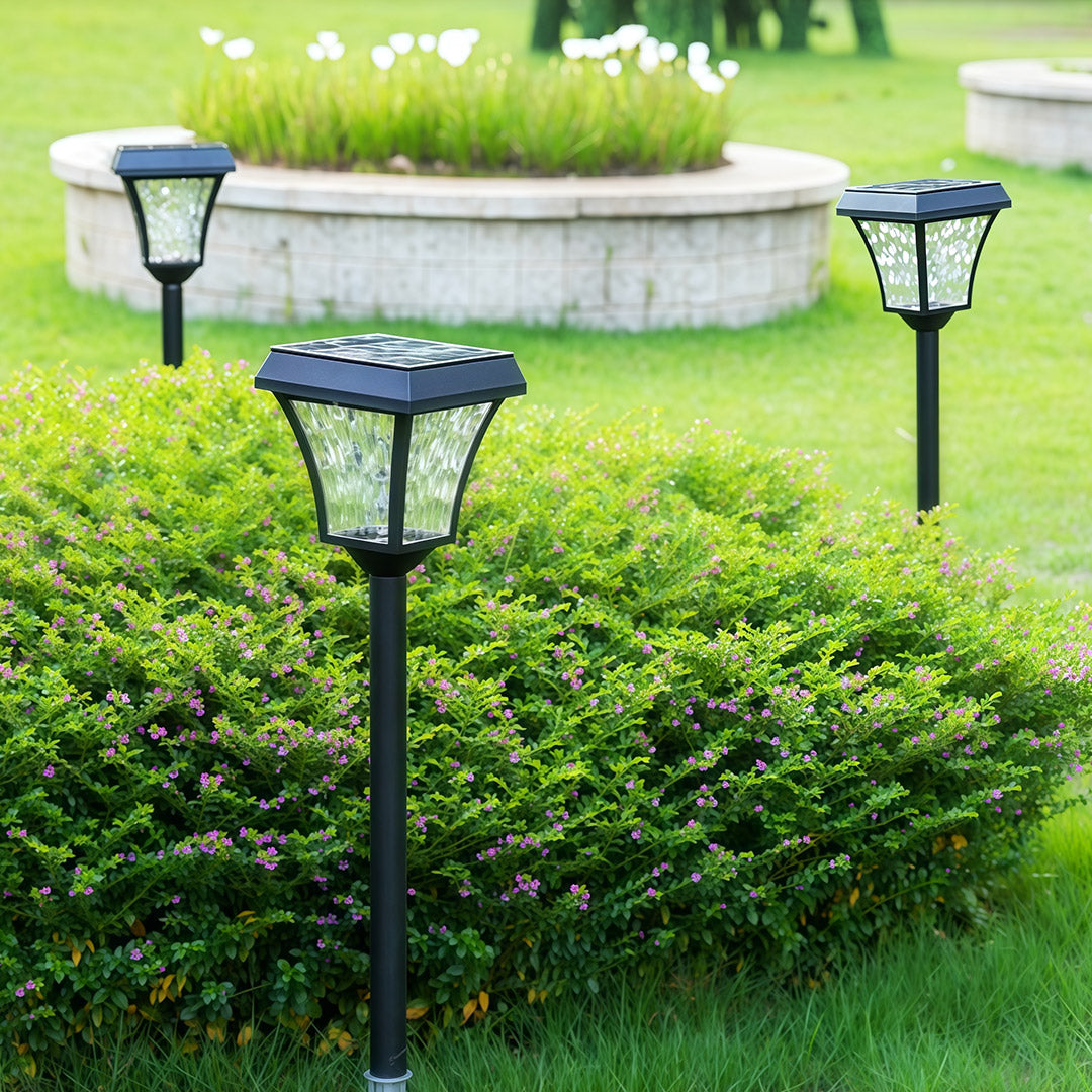 Daytime view of outdoor solar path lighting stakes installed around a lush green garden shrub.