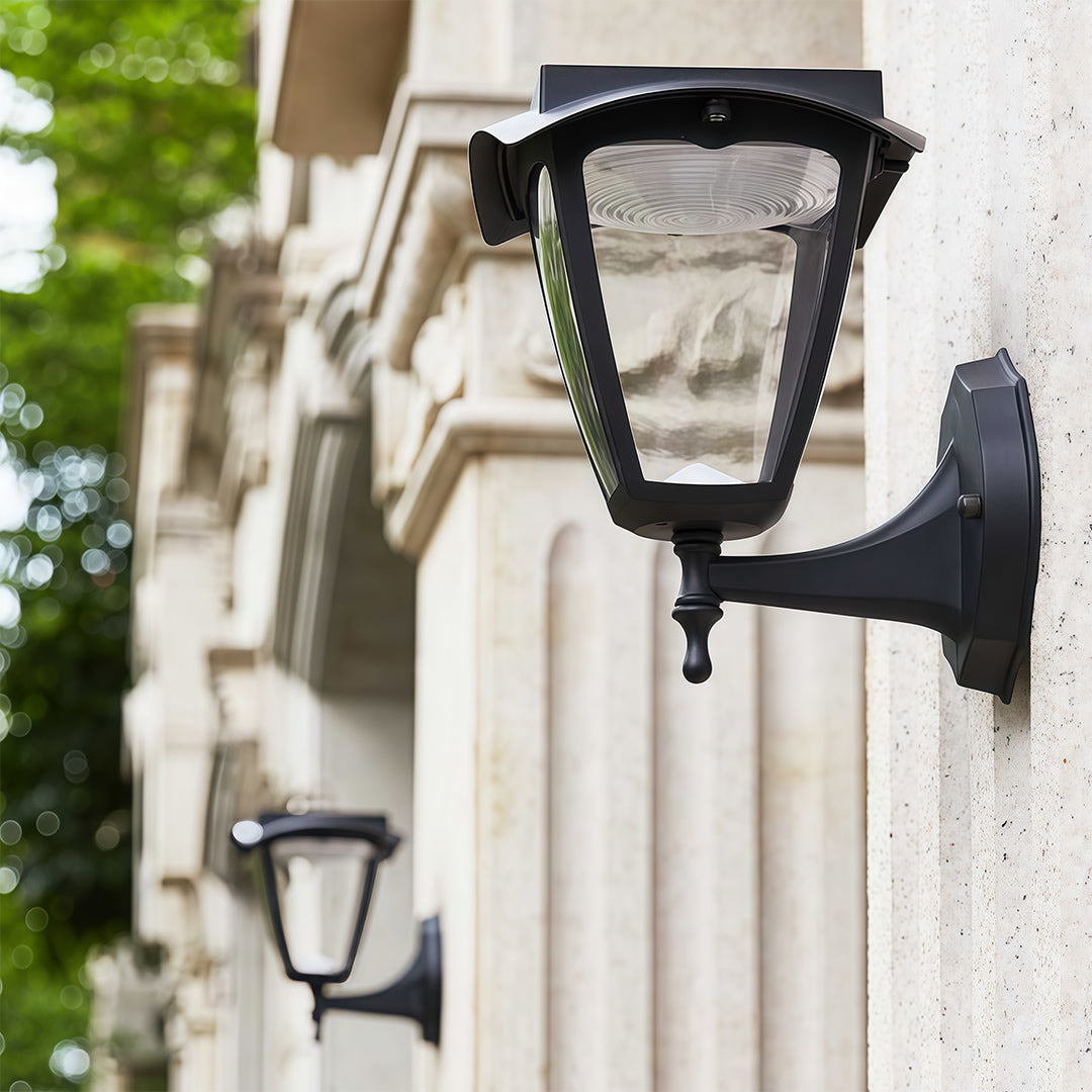 Daytime view of traditional outdoor wall lighting black sconces installed on ornate, light-colored stone columns.