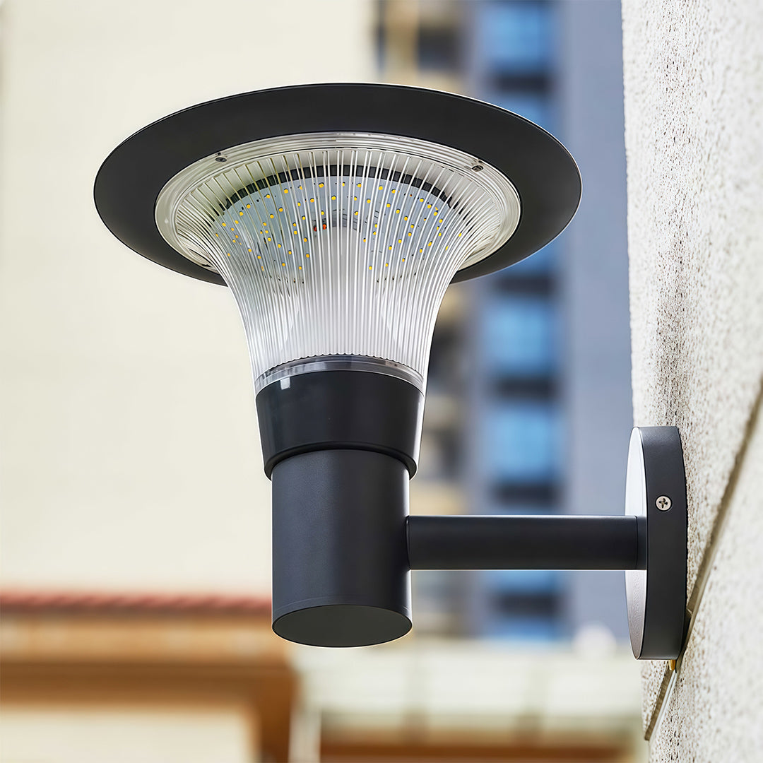 Daytime view of the black outdoor solar wall sconce highlighting its top solar panel and clear textured diffuser.