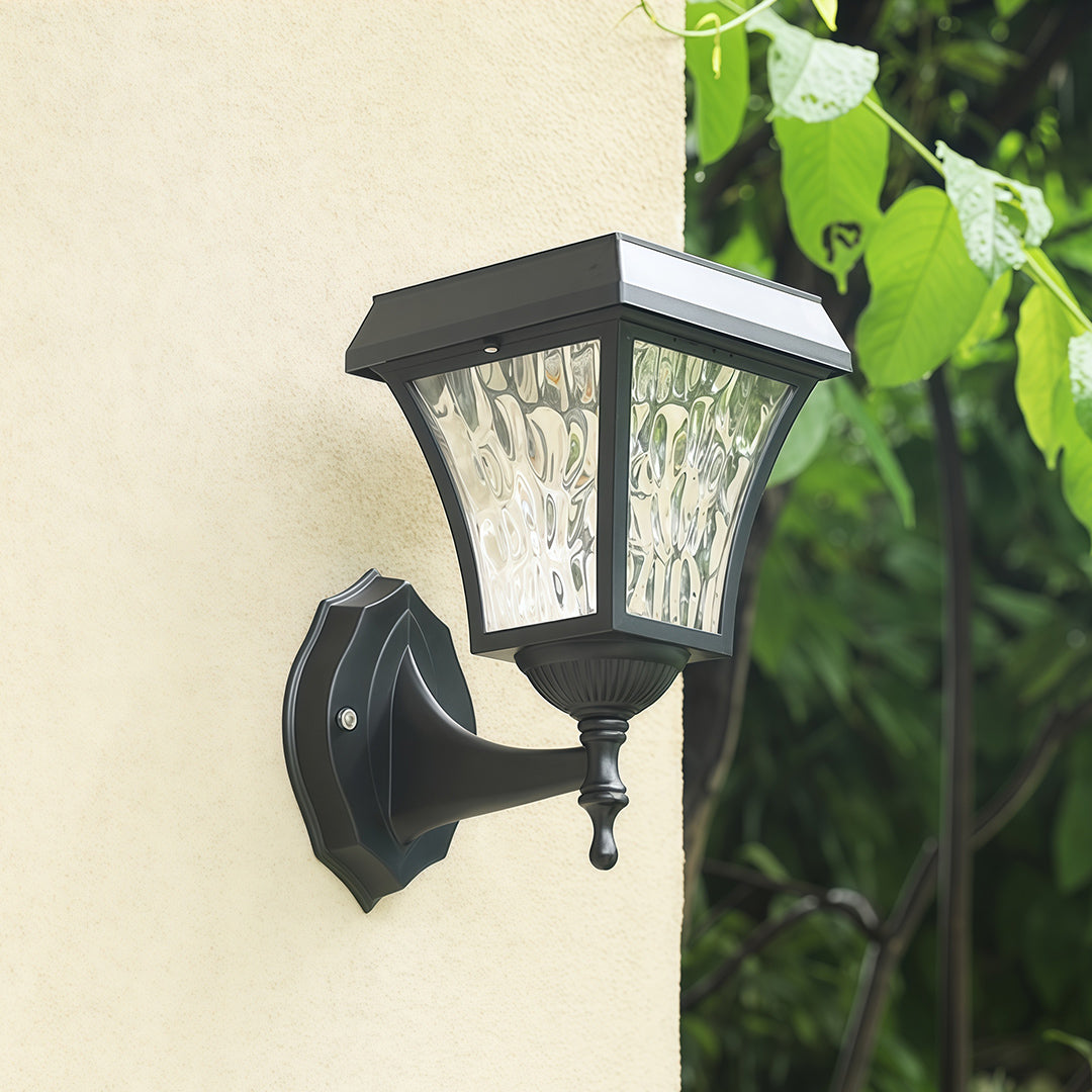 Daytime view of a black solar outdoor sconce light with textured glass installed on a stucco wall.