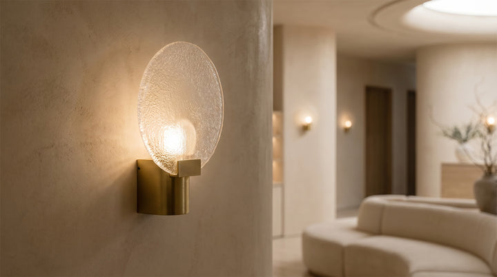Modern round wall light with a frosted glass shade and gold metal base, mounted beside a cozy bedroom headboard.
