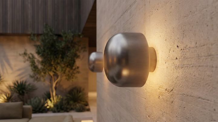 Modern LED outdoor wall lights illuminating the entrance of a white brick house with wooden doors.