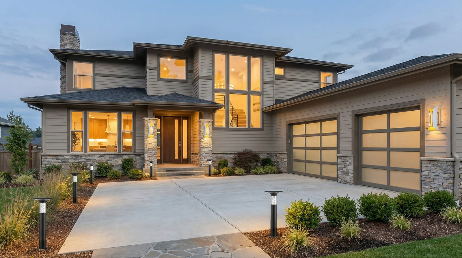 Modern two-story house facade at dusk featuring sleek black driveway lights illuminating the concrete entrance and landscape.