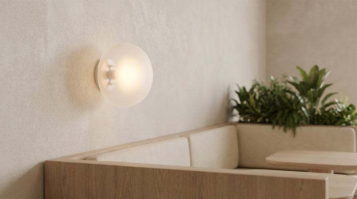 Pebbles wall lamp with a soft glow, mounted above a cozy wooden bed in a modern bedroom.
