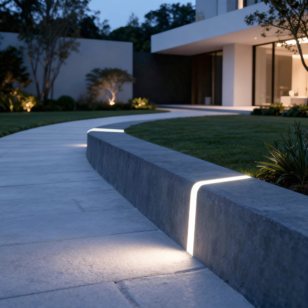 Deck lighting for steps installed on concrete retaining wall creating ambient illumination along residential driveway at dusk