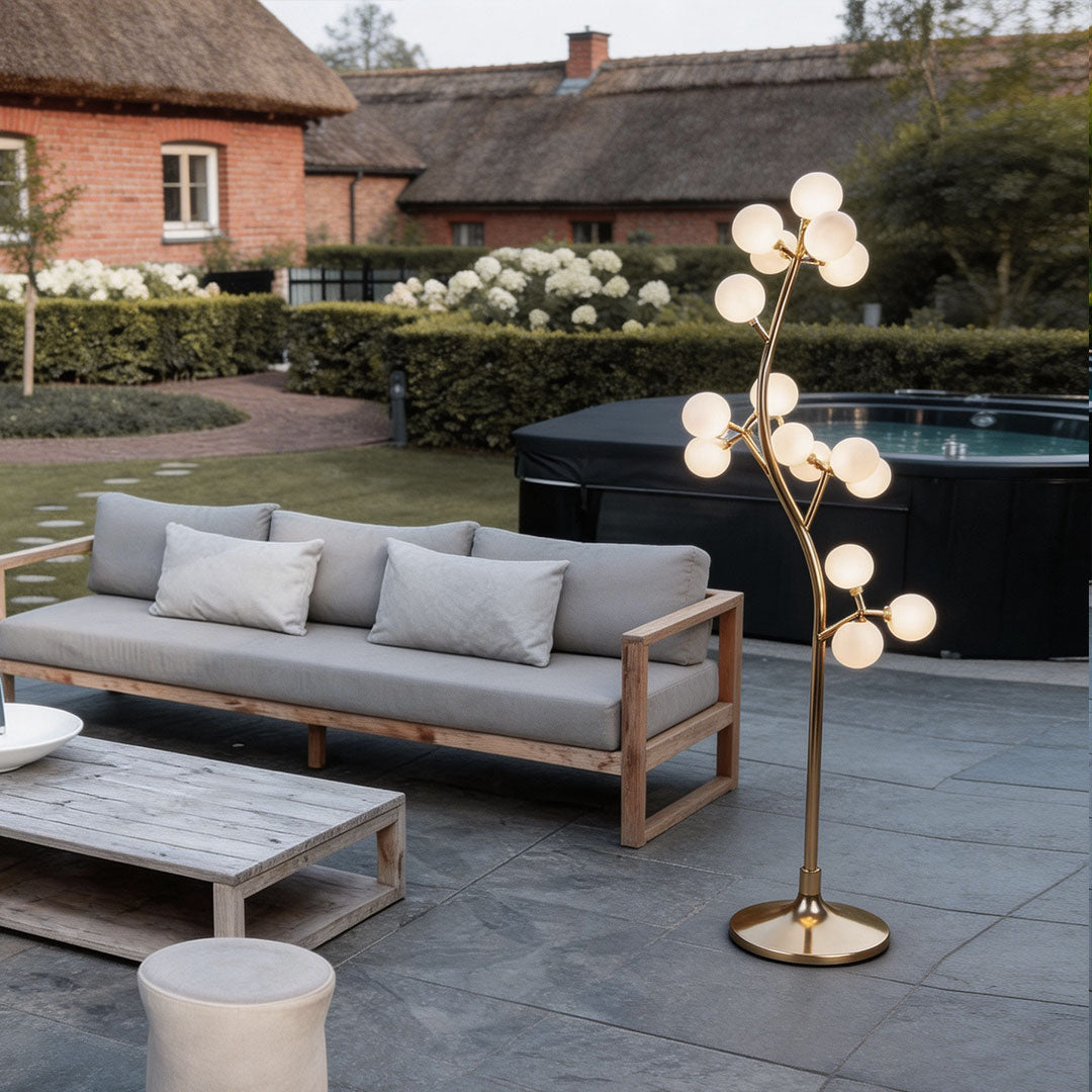 Decorate floor lamp with a modern tree design, providing warm illumination near a garden sofa.