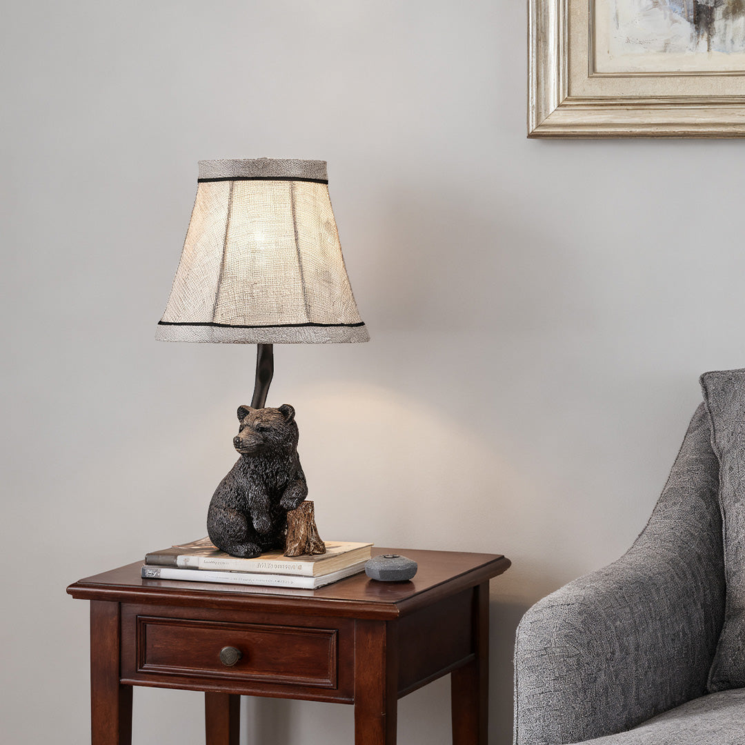 Decorative resin table lamp base molded into a detailed bear figure, illuminating a dark wood nightstand in a cozy living space.