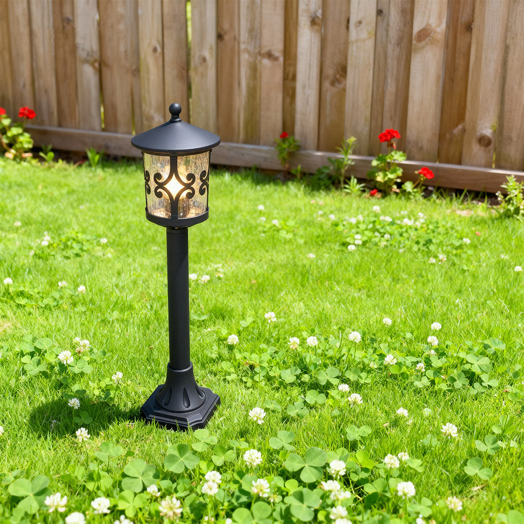 Decorative bollard LED light illuminating lush backyard lawn beside wooden privacy fence with flowers