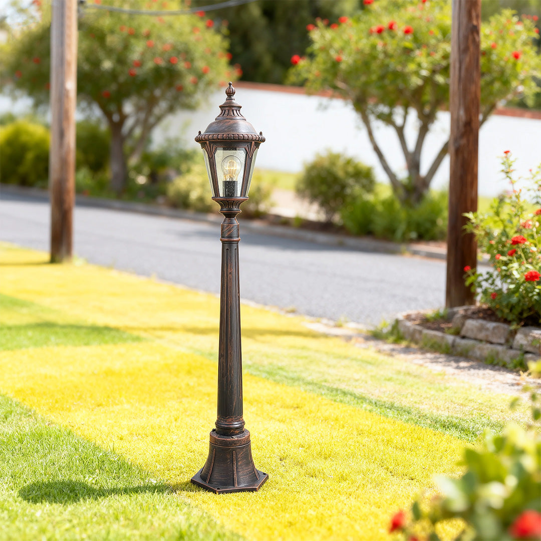 Decorative bollard light brightening residential driveway with manicured lawn and tree backdrop in daylight
