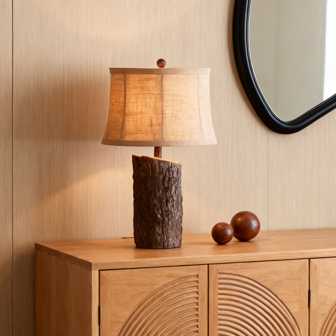 Decorative faux wood table lamp featuring a carved bark-like texture, sitting on a light wood accent cabinet.