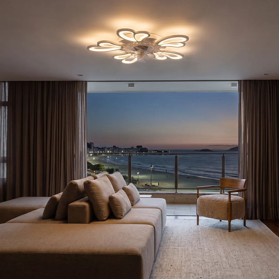 Decorative ceiling fans with lights glowing above a modern room with a sofa and ocean view at dusk.
