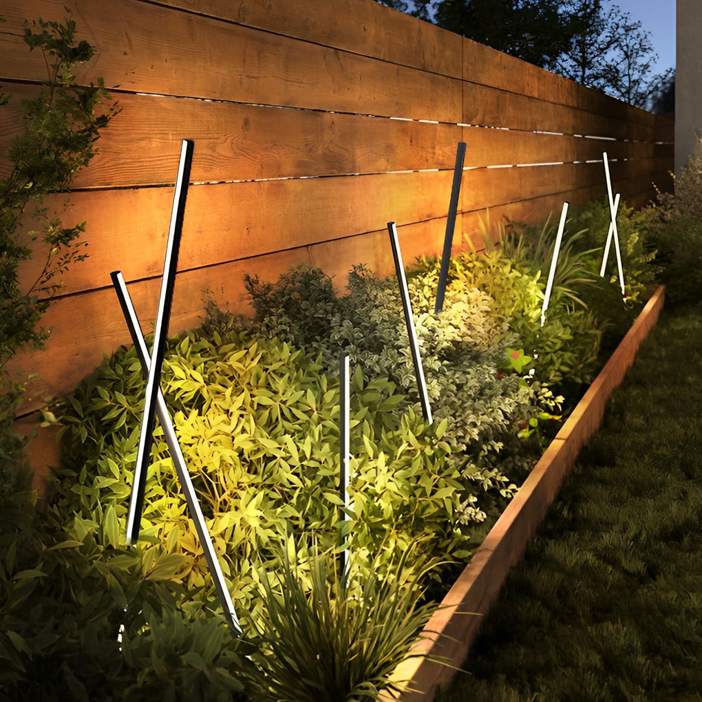 Angled decorative contemporary outdoor floor lamps highlighting landscape plants and wooden fencing.