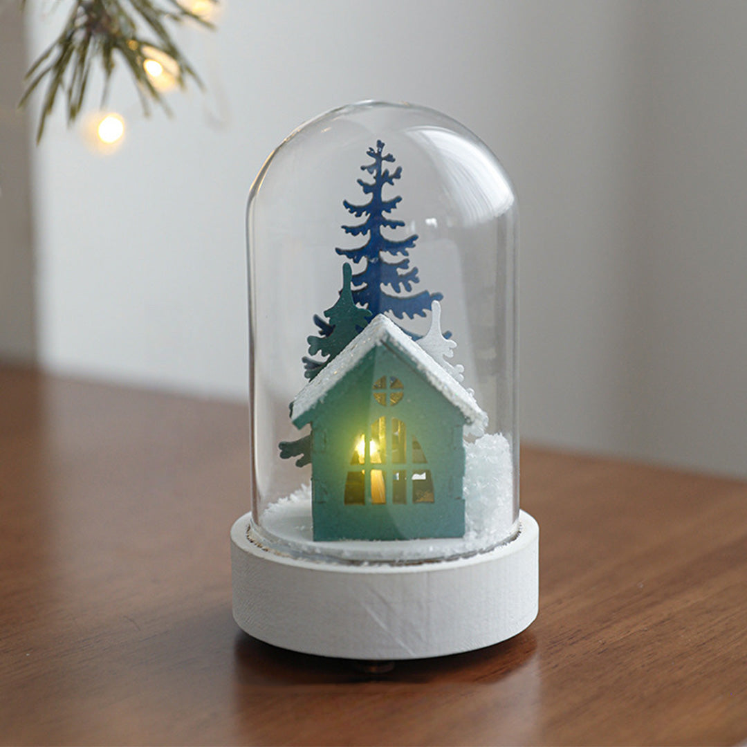 Decorative led table lamp on surface with white base featuring green house miniature and protective glass cloche