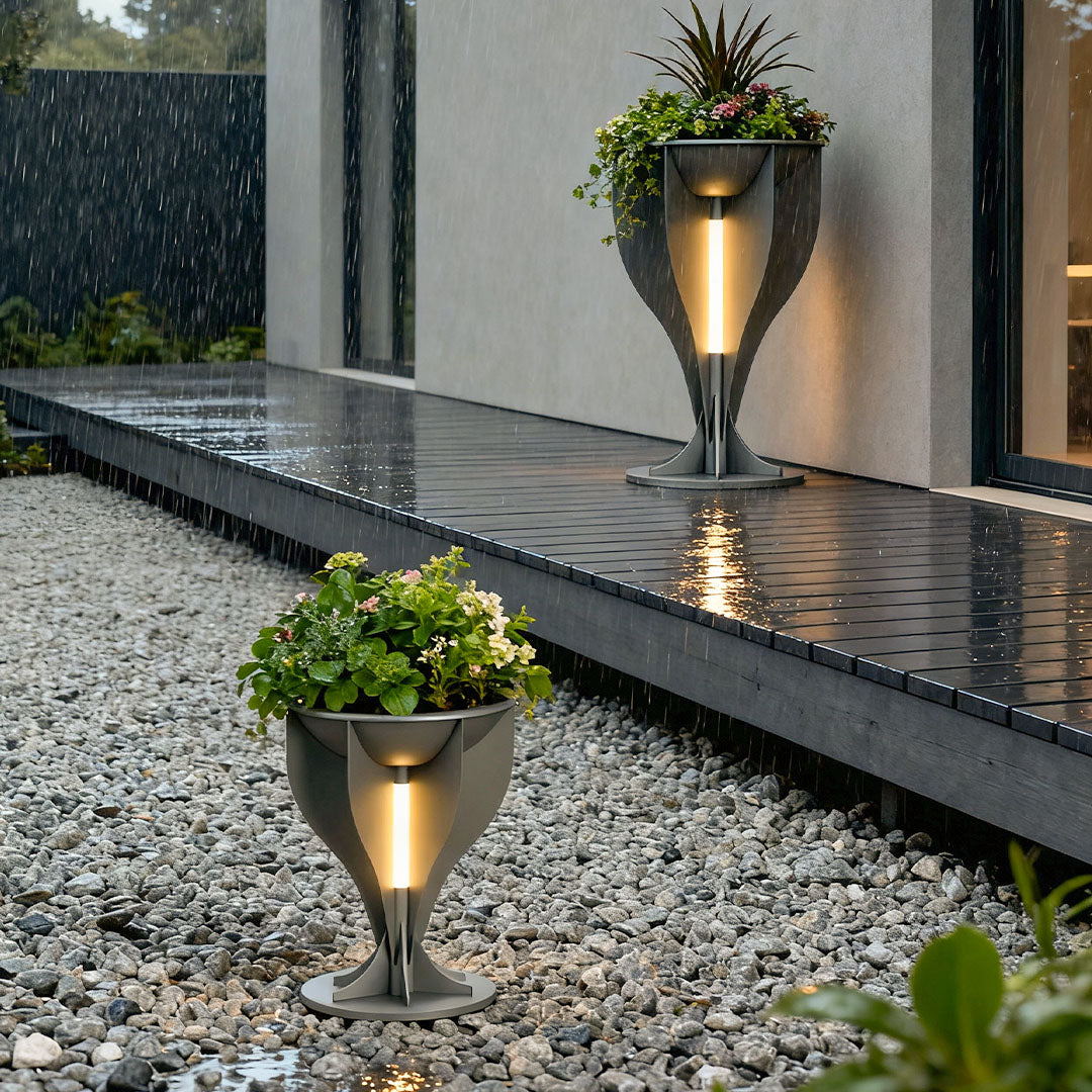 Two decorative lighted planter pots providing illumination on a wet modern walkway and gravel path.