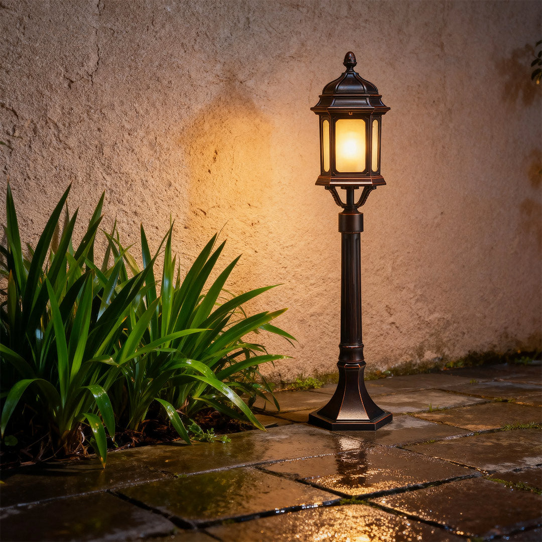 Decorative path bollard light with warm LED illumination against textured stucco wall near tropical plants