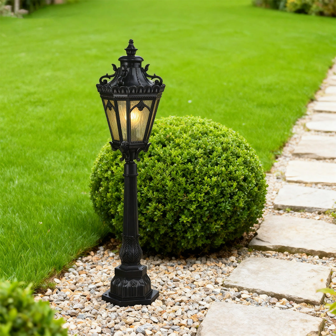 Decorative pathway lighting bollard illuminating vibrant green grass beside manicured round hedge