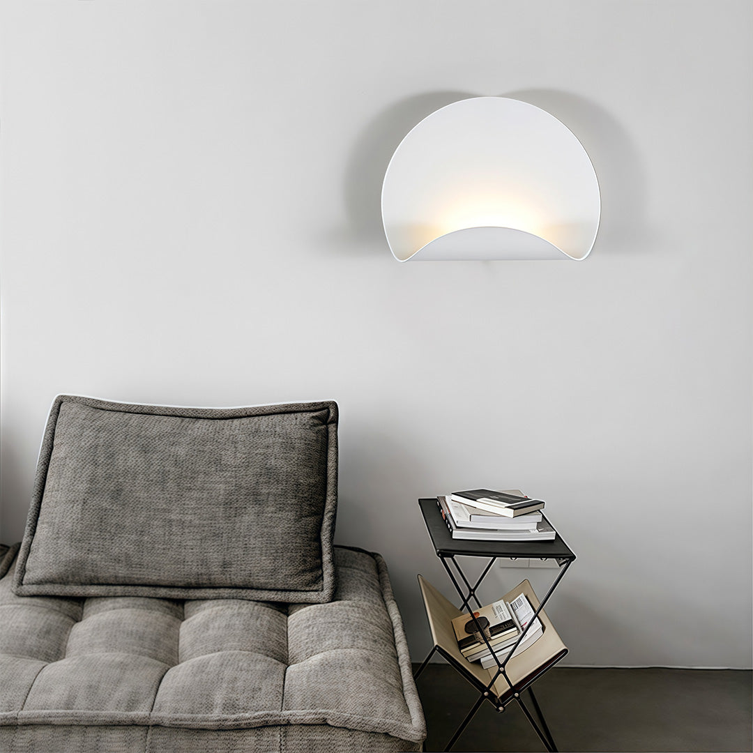 Decorative white wall lights mounted above a gray cushion bench, illuminating a dark accent table and books for reading.