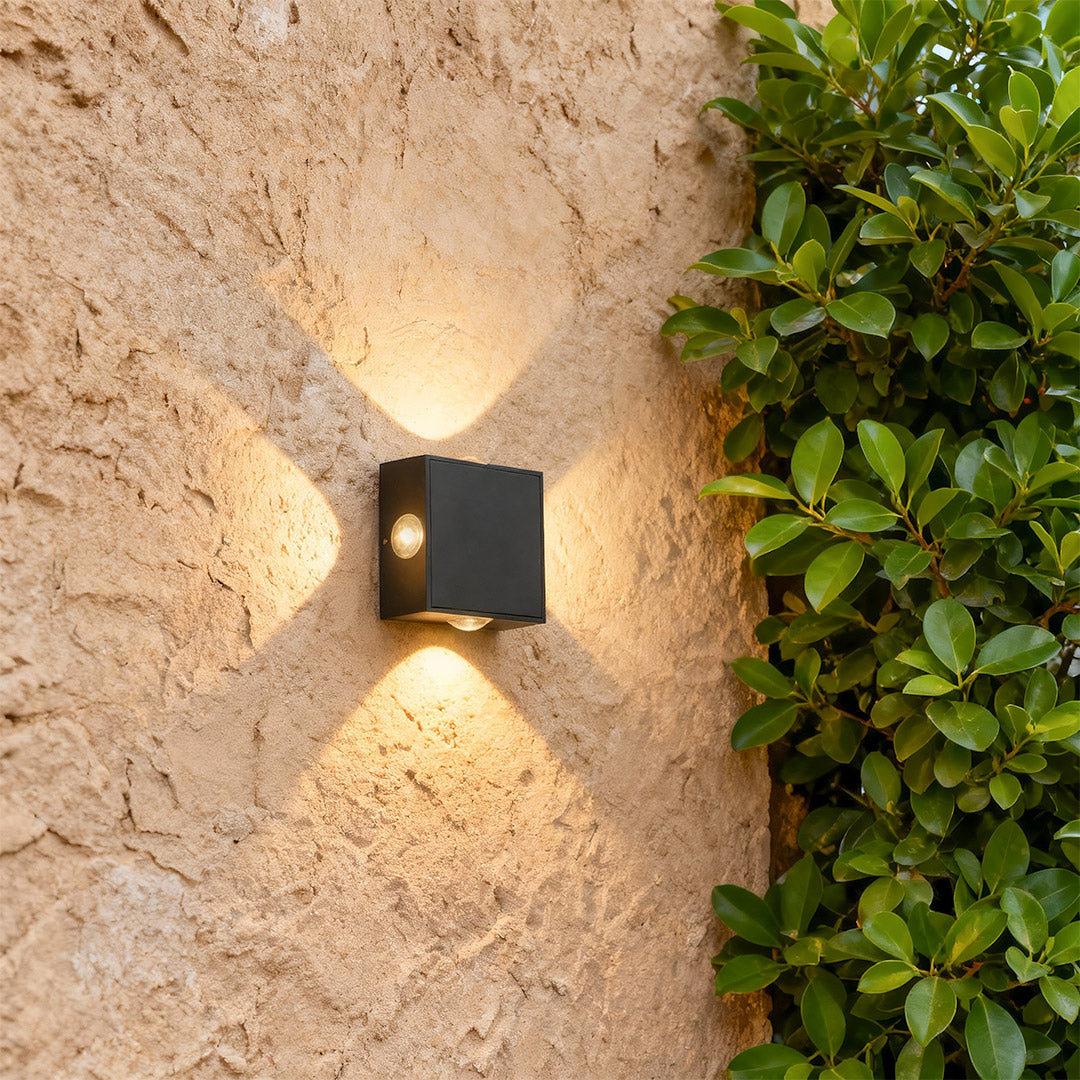 Designer black outdoor sconce light with glass shade chandelier aesthetic providing ambient uplighting and downlighting on textured exterior.