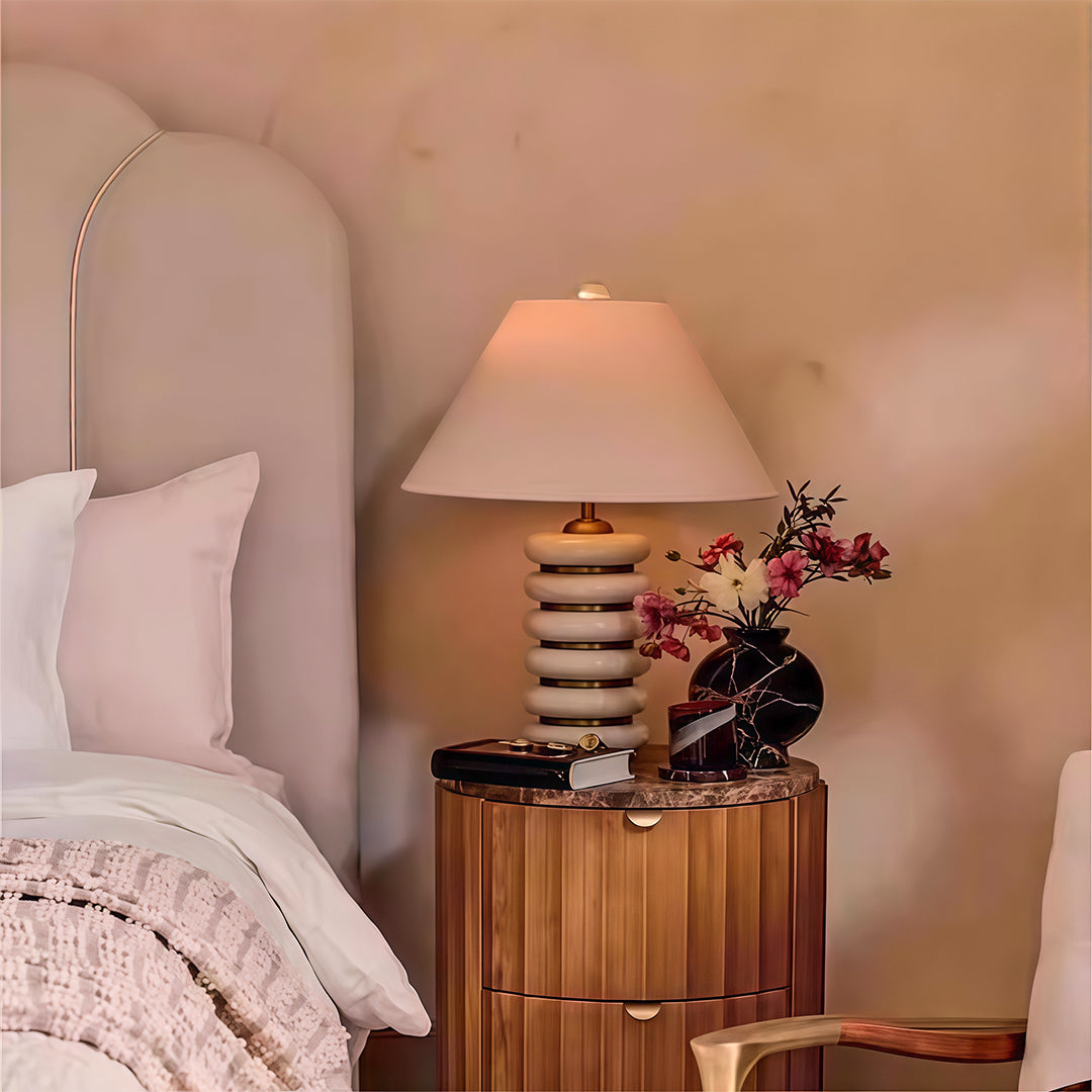 Designer cloth table lamp with glass shade chandelier aesthetic providing warm ambient glow on bedroom nightstand with textured base.