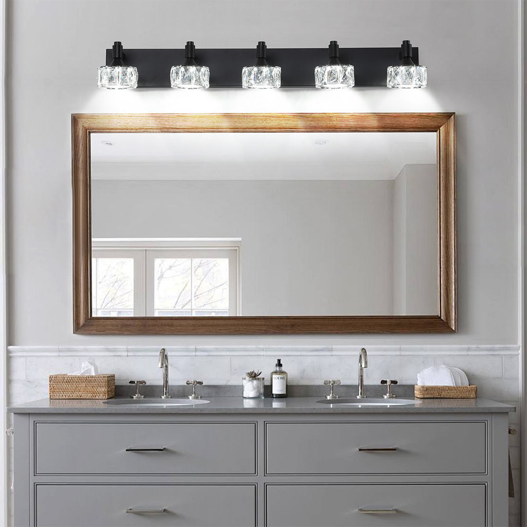Designer crystal bathroom vanity light with glass shade chandelier influence mounted above gray vanity with natural wood mirror frame.