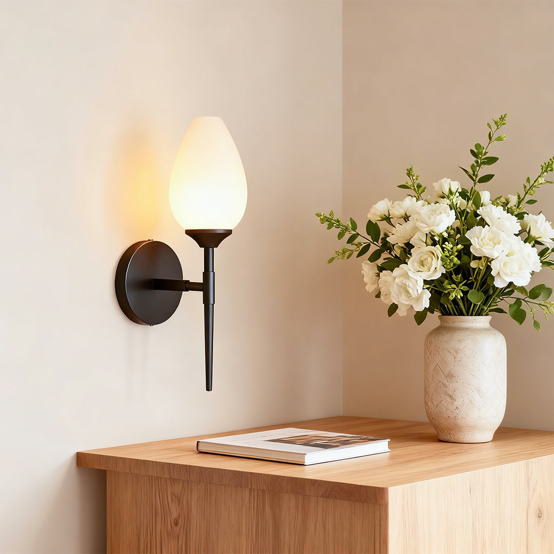 Designer glass wall lights featuring glass shade chandelier aesthetic providing ambient lighting beside entryway with decorative flowers.