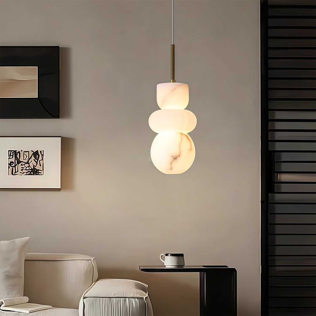 Designer minimalist pendant light featuring glass shade chandelier aesthetic creating soft glow beside burgundy upholstered bed.