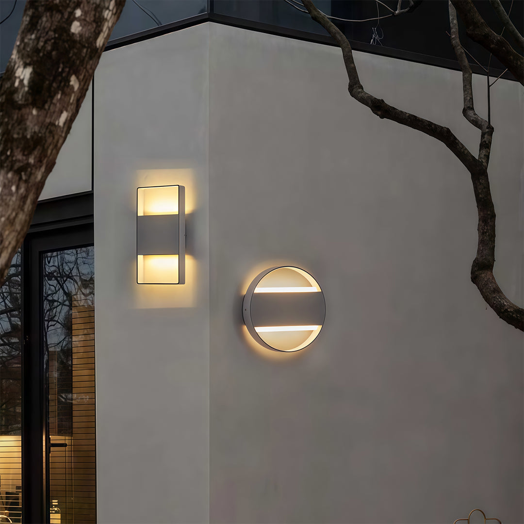 Designer mixed wall mount exterior lights with glass shade chandelier styling in round and rectangular combinations on gray wall.