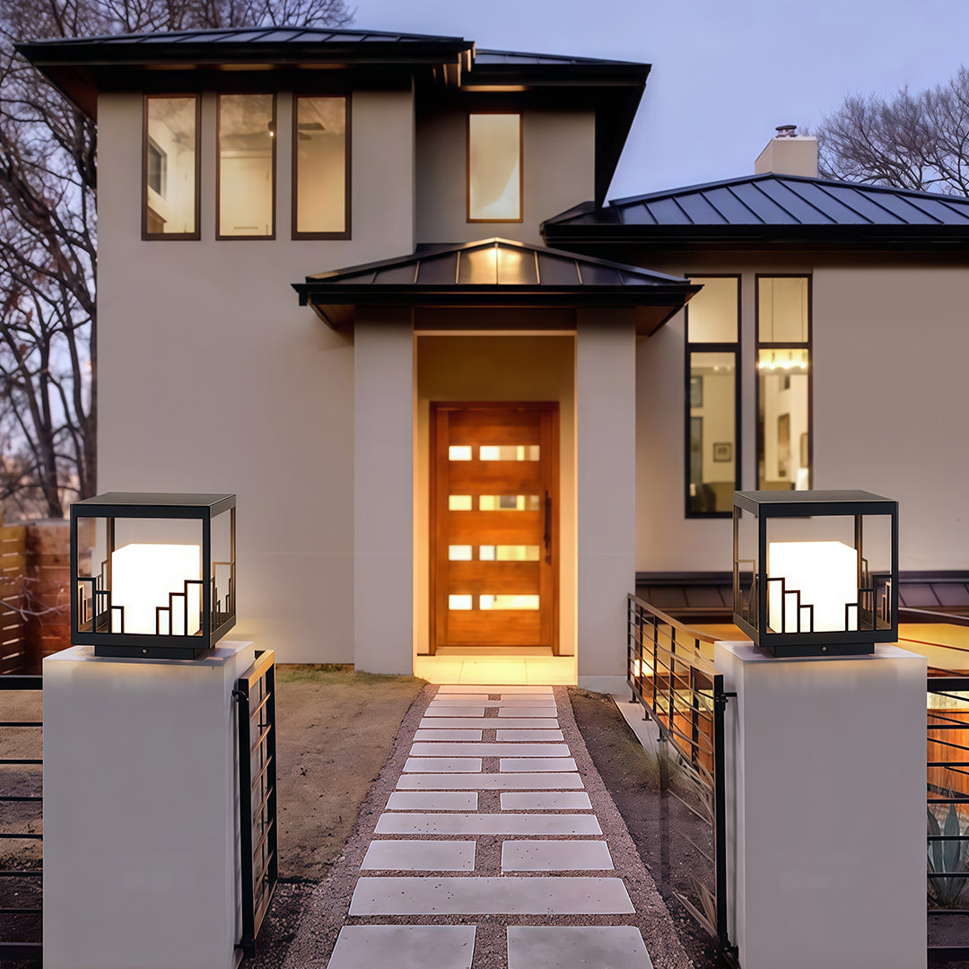 Designer outdoor pillar light featuring glass shade chandelier styling illuminating contemporary walkway with warm ambient light.