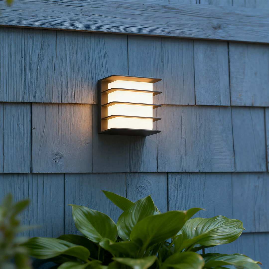 Designer square LED wall lights with glass shade chandelier aesthetic creating beautiful louvered light effect on rustic blue siding.