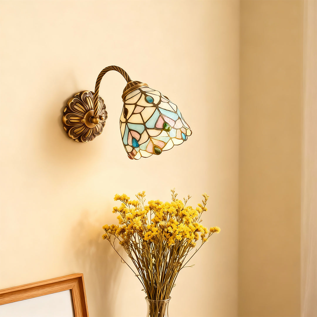 Designer stained glass wall sconce lighting featuring glass shade chandelier aesthetic creating warm glow beside decorative flowers.