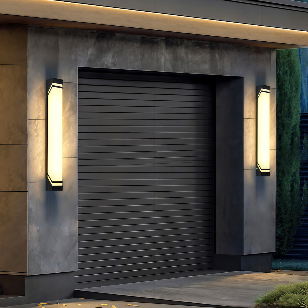Designer wall mounted exterior lights with glass shade chandelier styling illuminating modern garage door entrance at dusk.