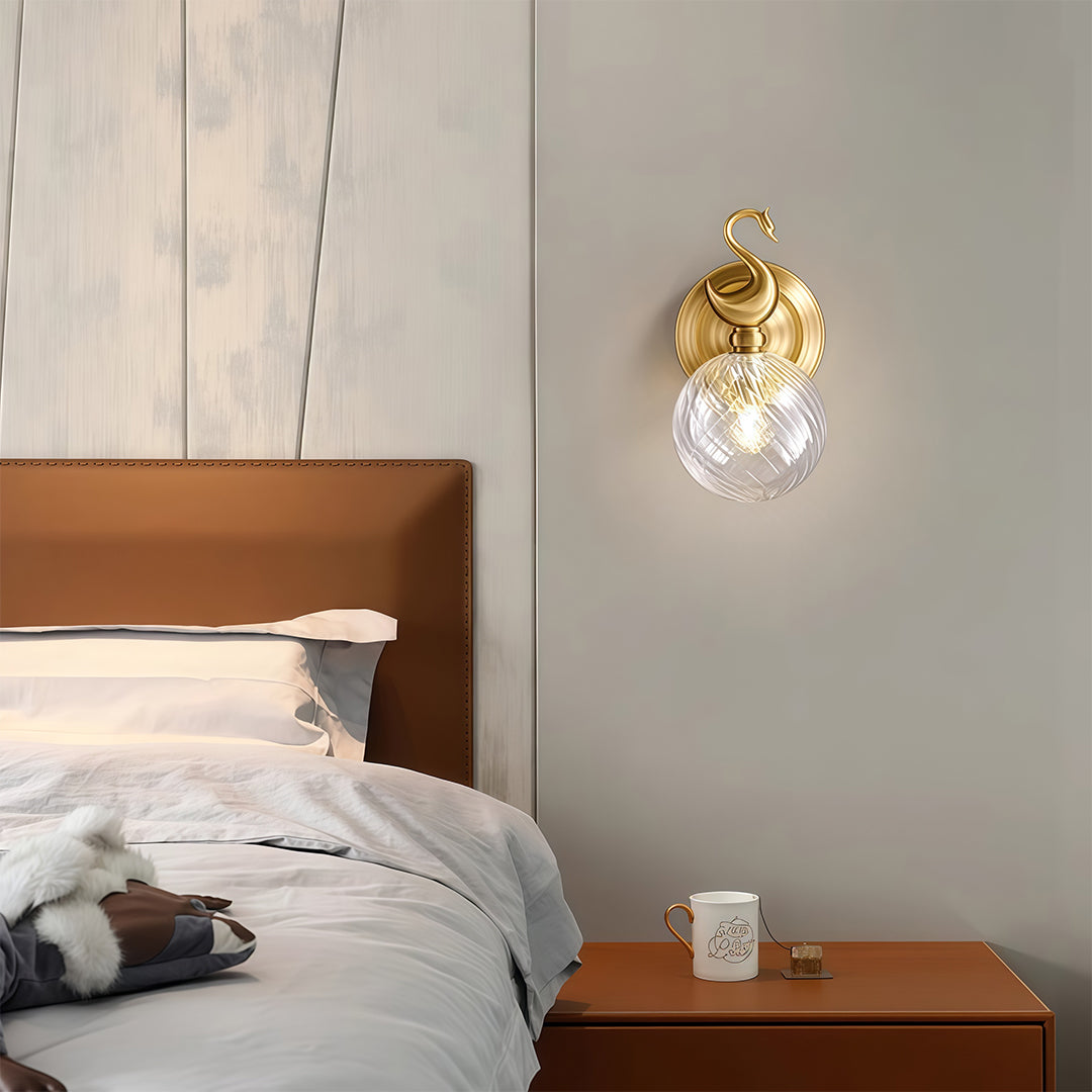 Designer wall mounted LED light featuring glass shade chandelier aesthetic illuminating contemporary bedroom with orange accent pillow.