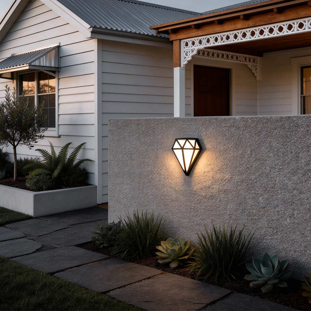 Diamond shape wall light with a modern design, mounted on a stone wall beside a garden.