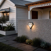 Diamond shape wall light with a modern design, mounted on a stone wall beside a garden.