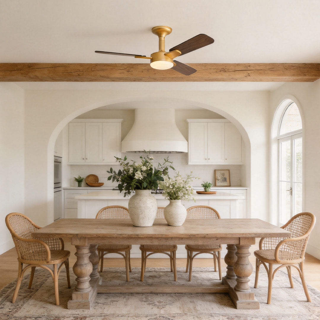 Copper ceiling fan with light installed above a dining area with dark wood blades and warm lighting.