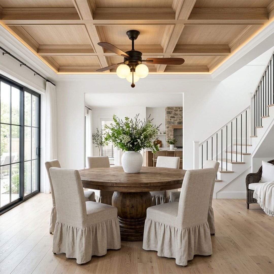Indoor ceiling fan with light installed above a dining table beneath a decorative coffered ceiling.