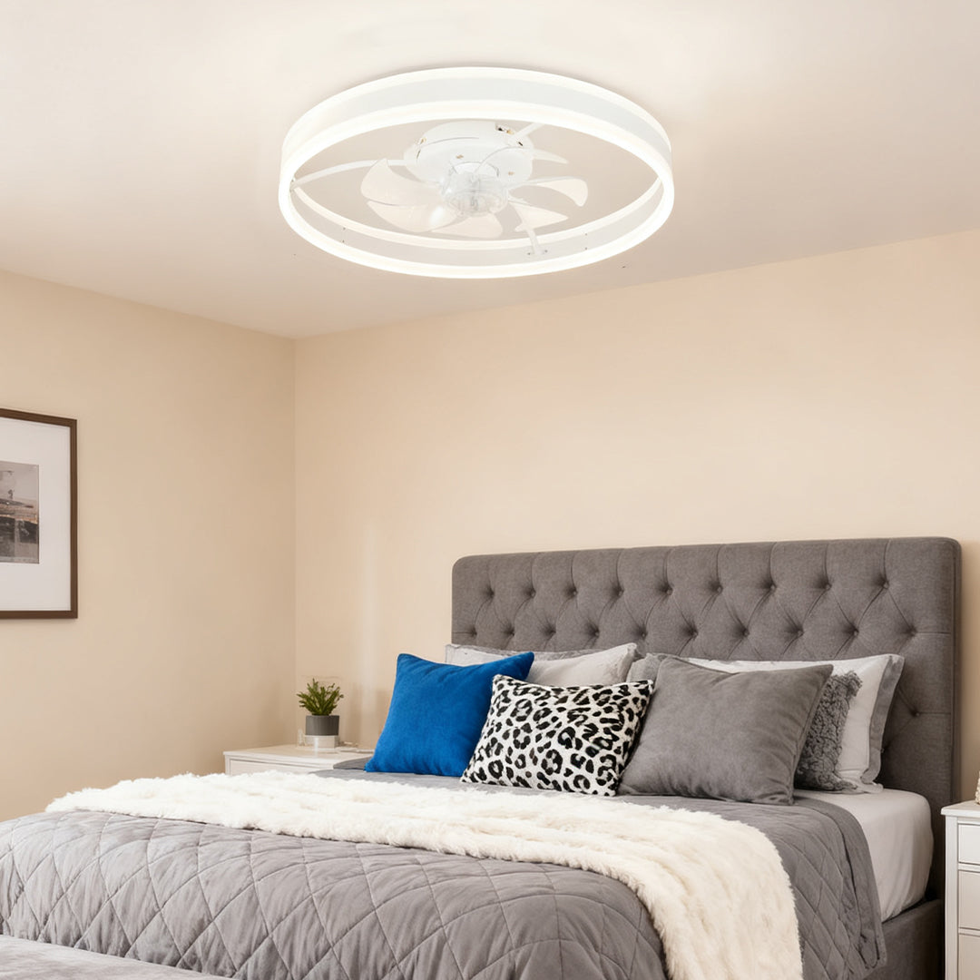 Discreet modern white ceiling fan with light installed in a cozy bedroom with a grey tufted headboard and blue accent pillows. 