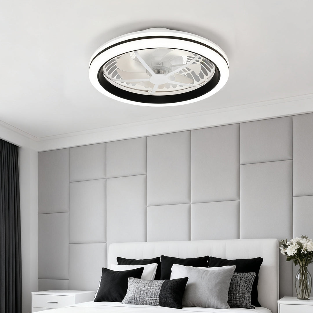 Discreet circular white flush mount ceiling fan with light above a bed with a plush grey paneled headboard in a contemporary bedroom. 